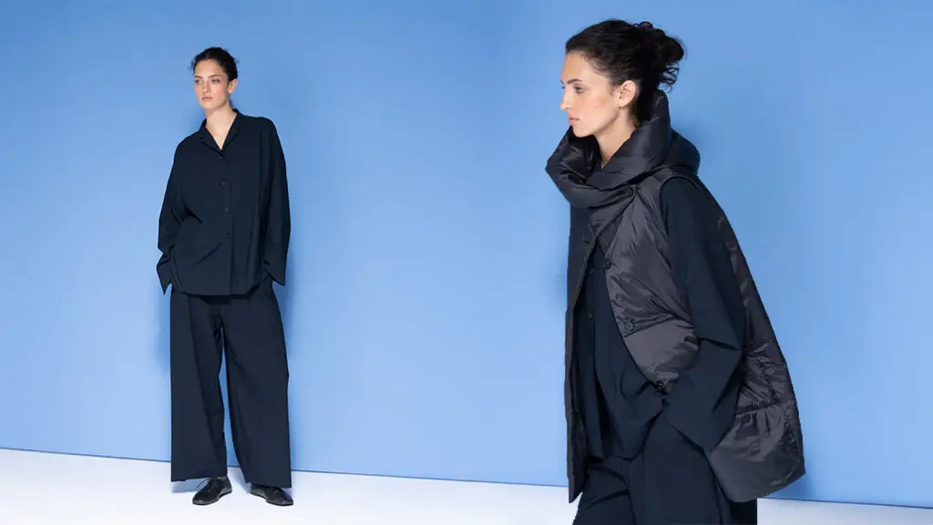 Žena předvádějící černý minimalistický outfit na modrém pozadí