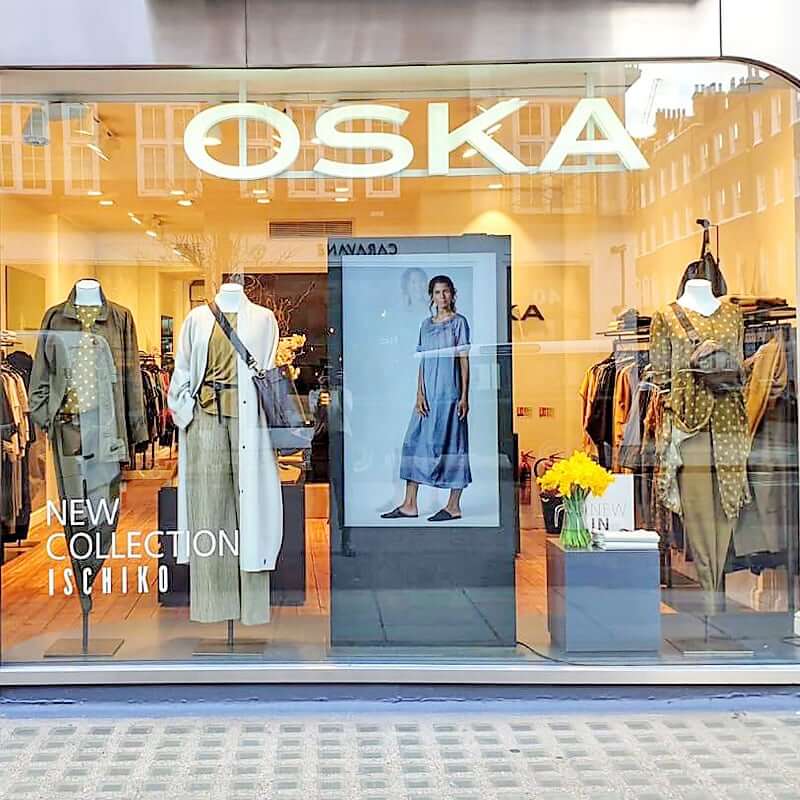 Mannequins in a boutique window display neutral-toned outfits, including olive trousers and a white coat.