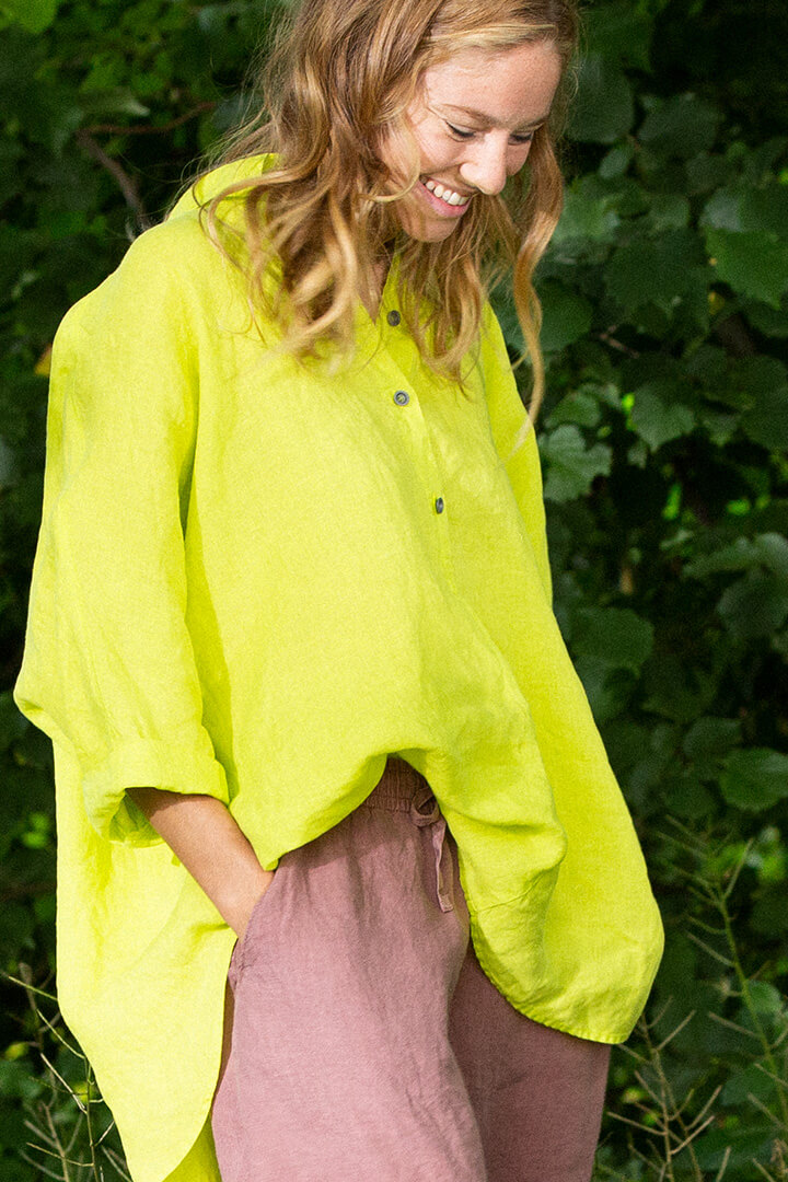 Une femme vêtue d'une chemise en chanvre OSKA de couleur vert citron vif, au milieu de la végétation