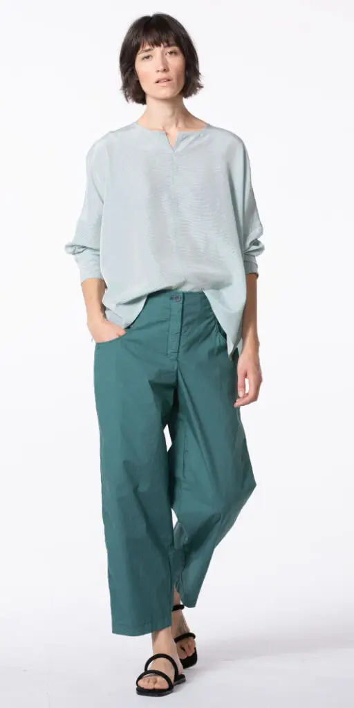 Model wearing a light blouse and teal pants.