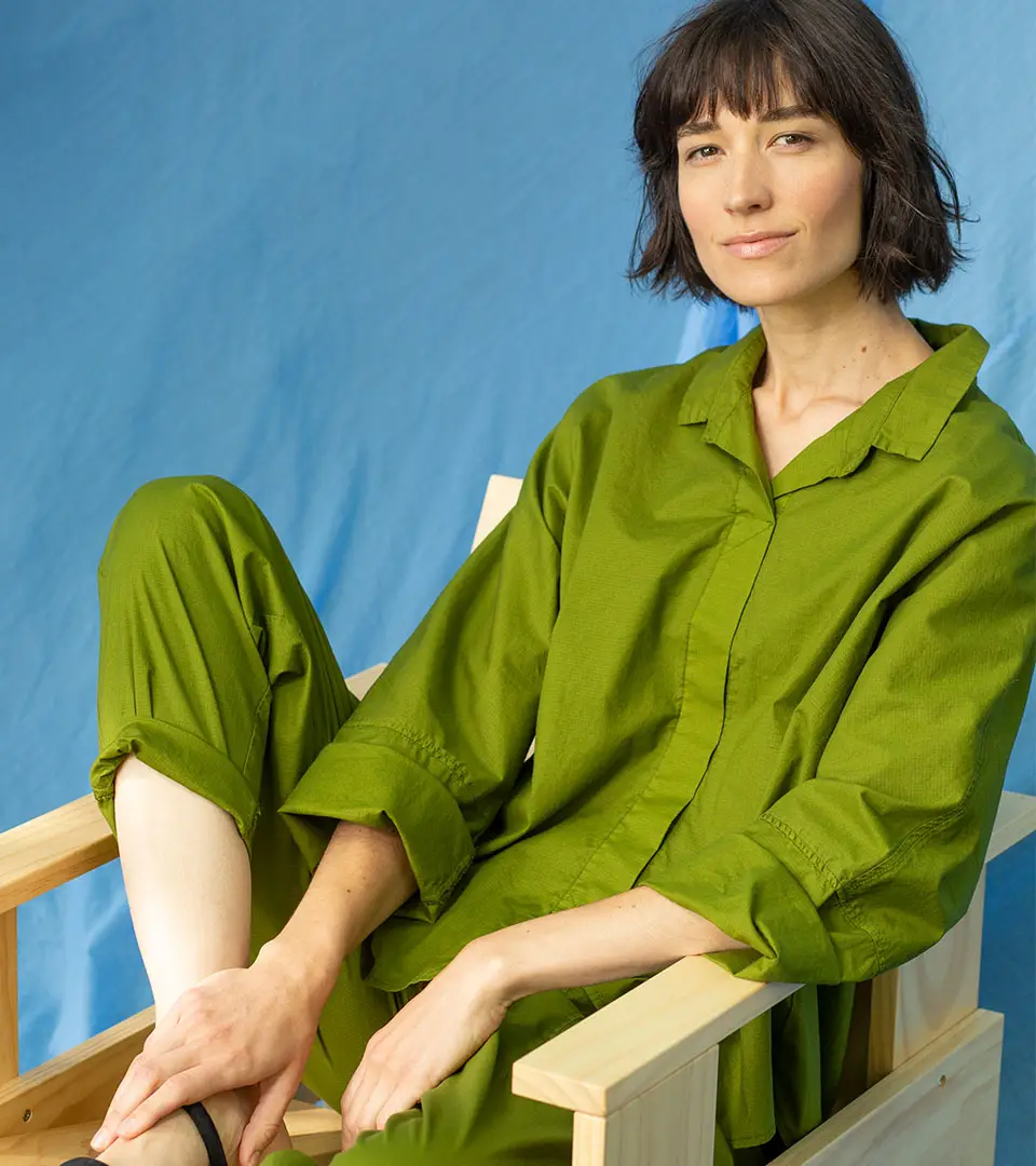 Woman in green attire seated on wooden chair.