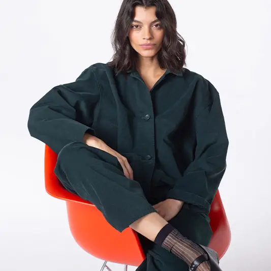 Model sitting in stylish green outfit on chair.
