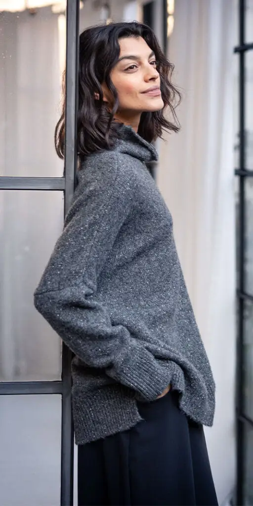 Woman in cozy sweater leaning against window.