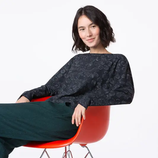 Woman seated in modern chair, wearing patterned top.