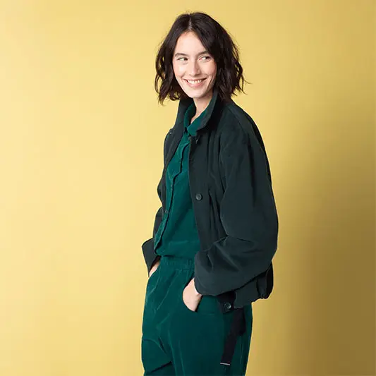 Woman smiling in green outfit against yellow background.