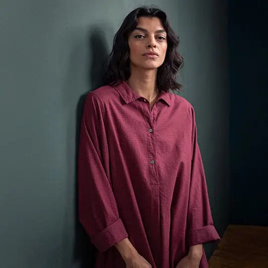 Person wearing a loose burgundy shirt, leaning against wall.