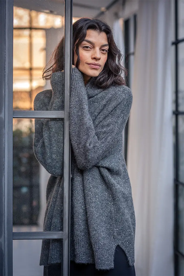 Person in cozy sweater leaning by window.