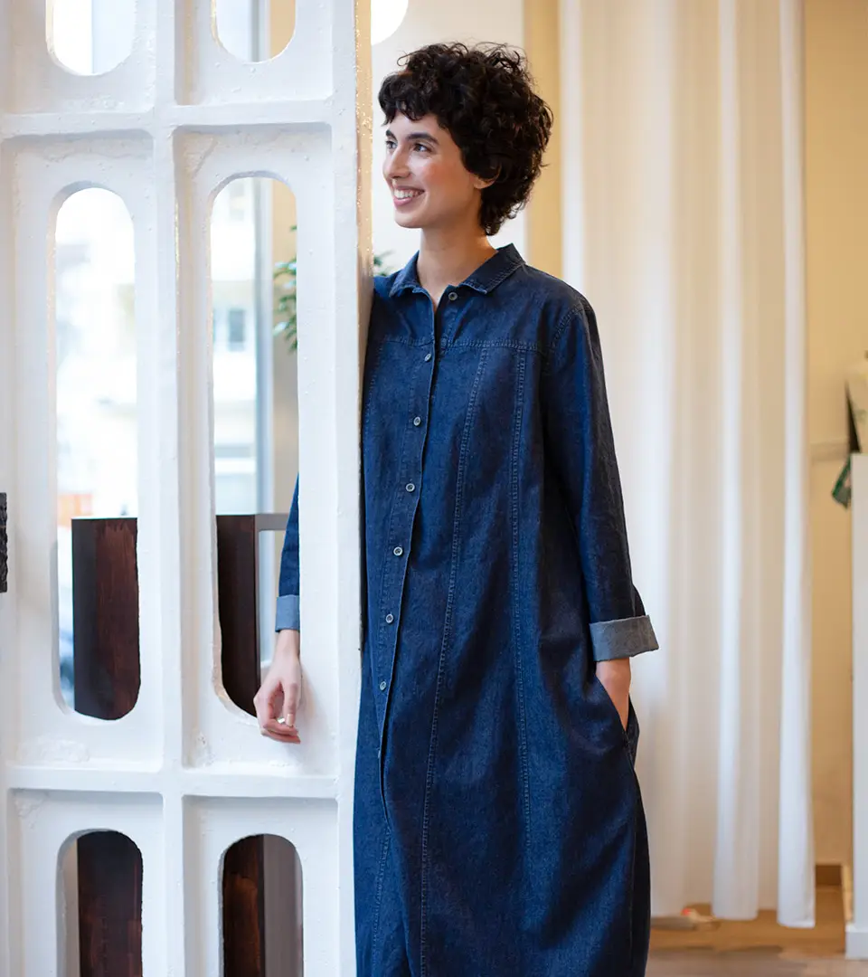 Smiling woman in denim dress by a wall