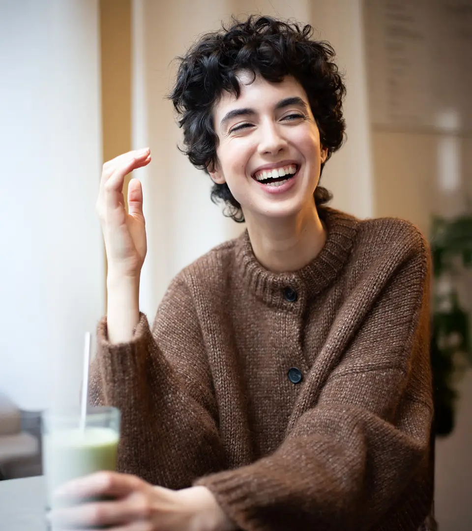 Young woman laughing with a drink in hand.
