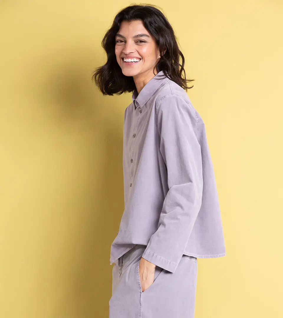 Woman in purple shirt smiling against yellow background.