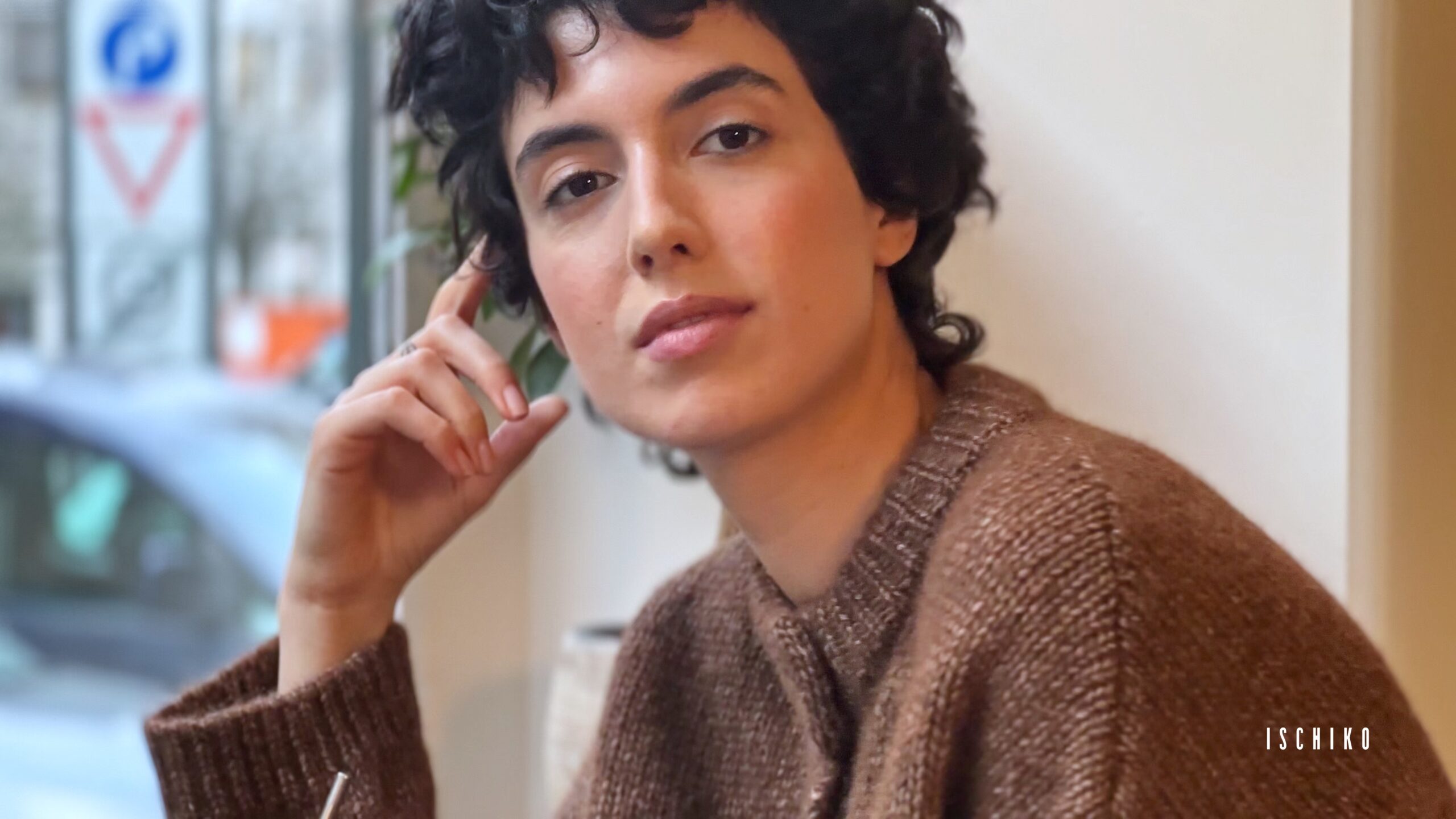 Person with dark curly hair in a brown sweater.