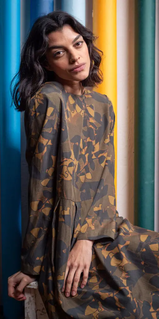 Model in patterned dress against colorful background.