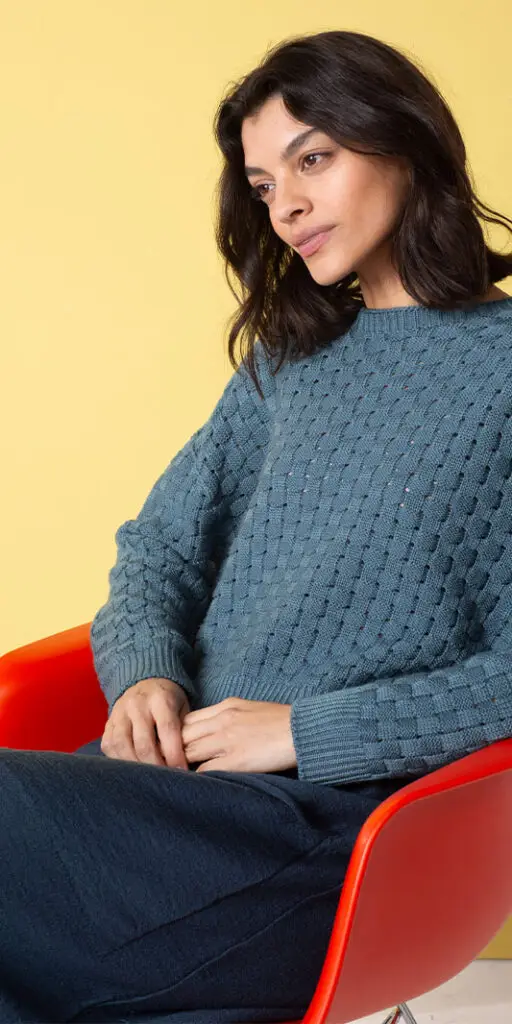 Woman seated in blue sweater and skirt.