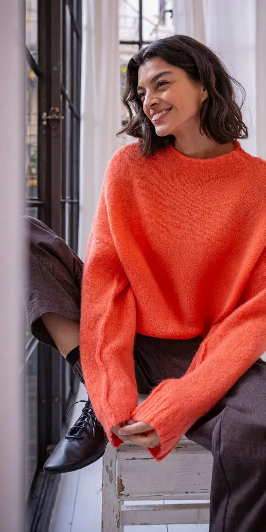 Femme souriante portant un pull orange à l'intérieur.