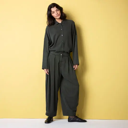 Woman in oversized dark outfit against yellow background.