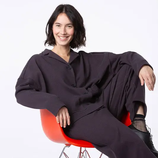 Smiling woman in stylish outfit on chair.