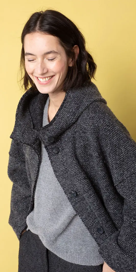 Femme souriante vêtue d'une veste grise élégante.