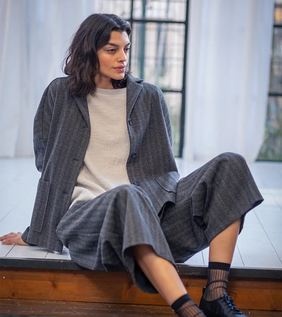 Person wearing stylish gray outfit, seated indoors.