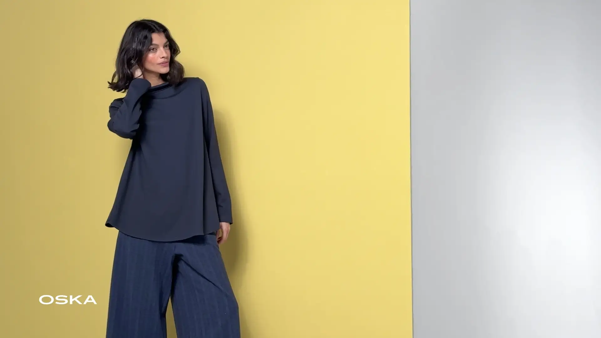 Woman posing in stylish outfit against yellow background.