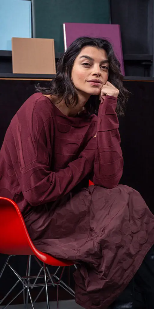 Woman sitting in a red chair, thoughtful pose.