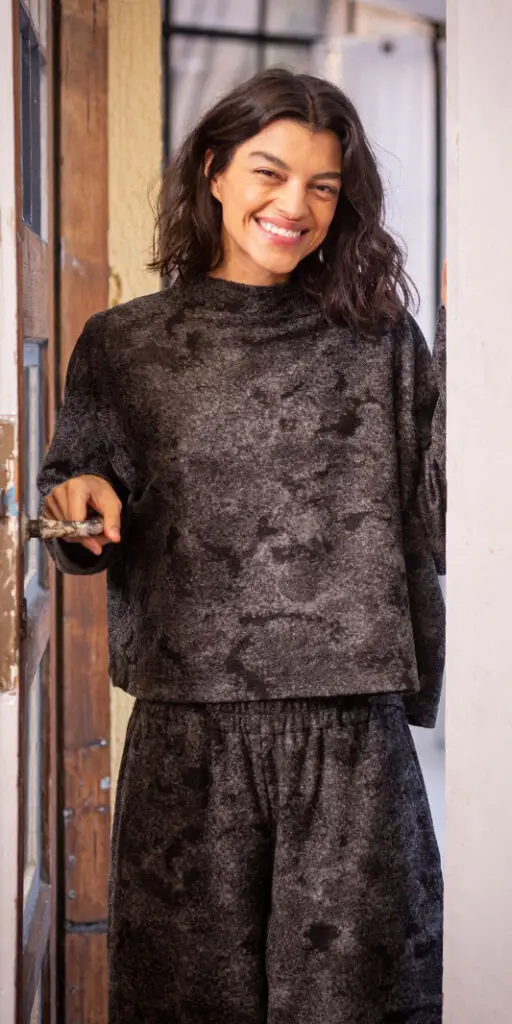Smiling person in casual gray outfit at doorway.