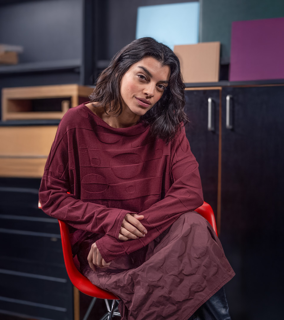 Woman seated, wearing a relaxed burgundy outfit.