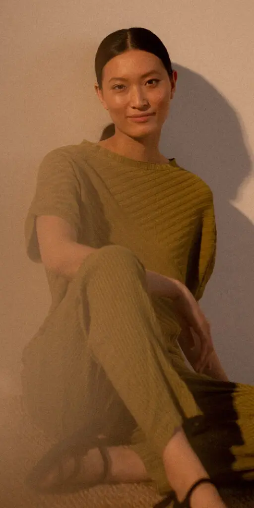 Woman in green outfit sitting elegantly.