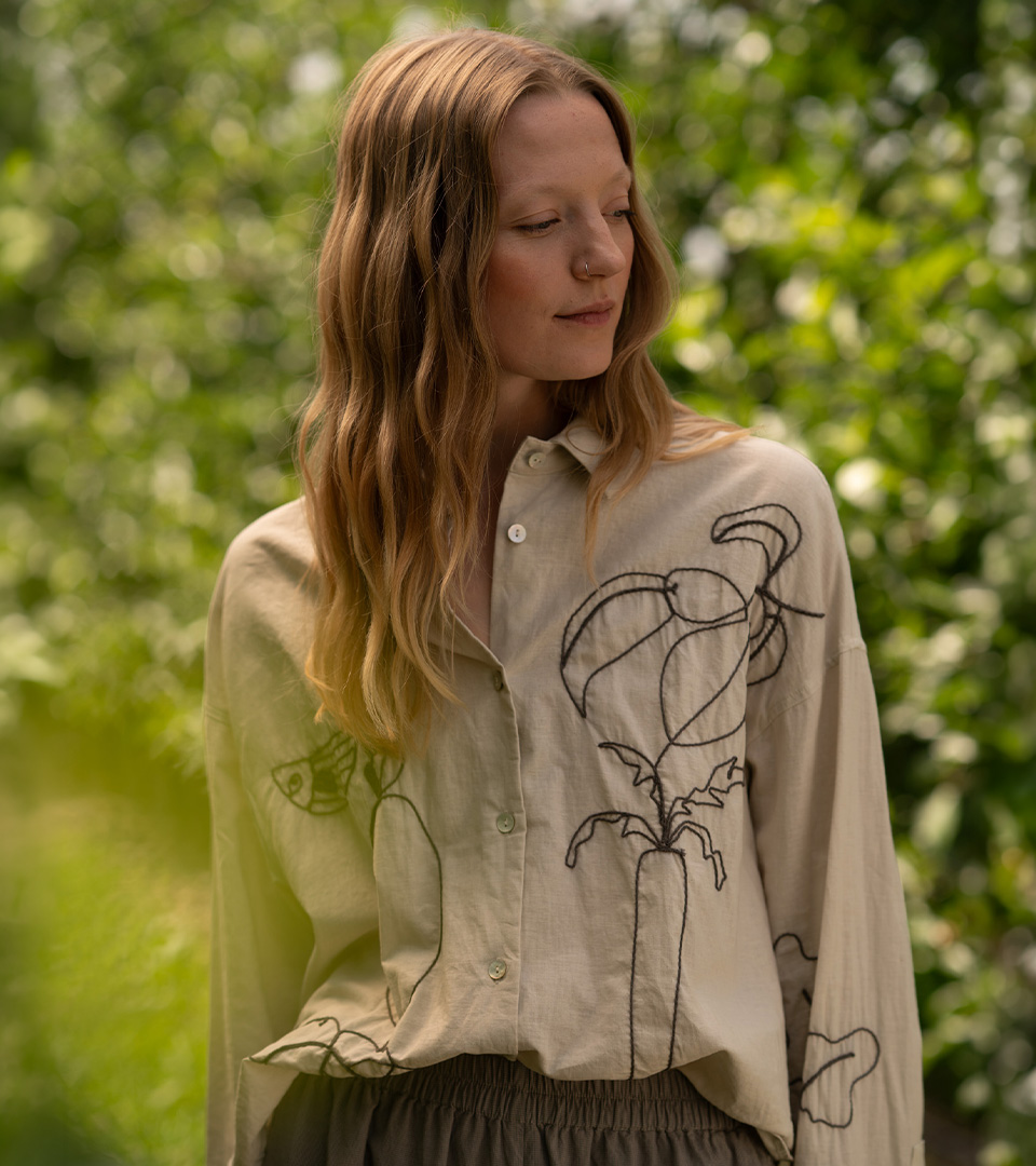 Person in embroidered shirt surrounded by greenery
