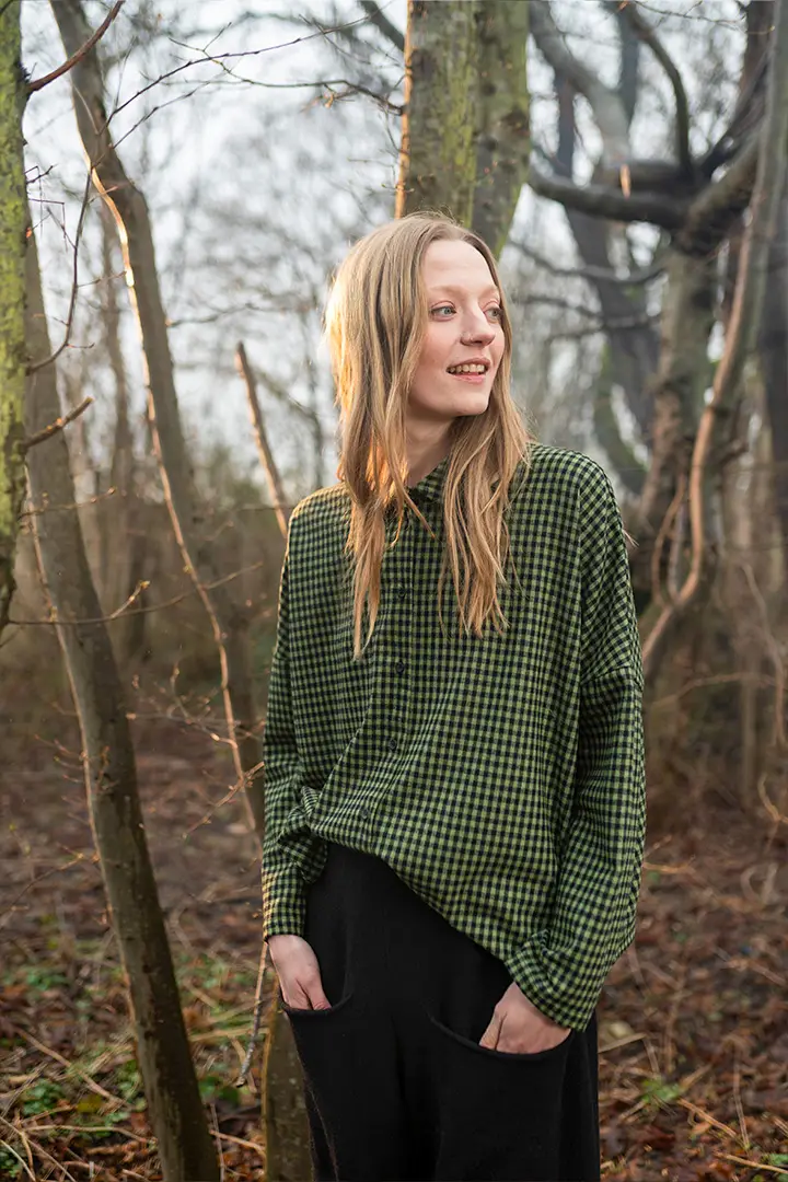 Femme en chemise à carreaux verte debout dans les bois