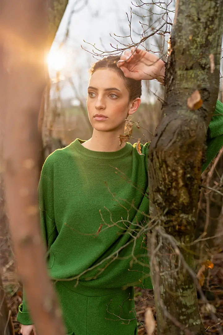 Woman in green sweater among trees at sunset