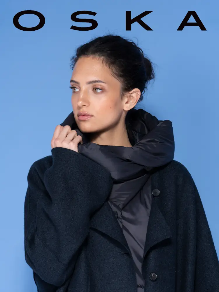 Frau in dunklem Mantel und Daunenschal vor blauem Hintergrund