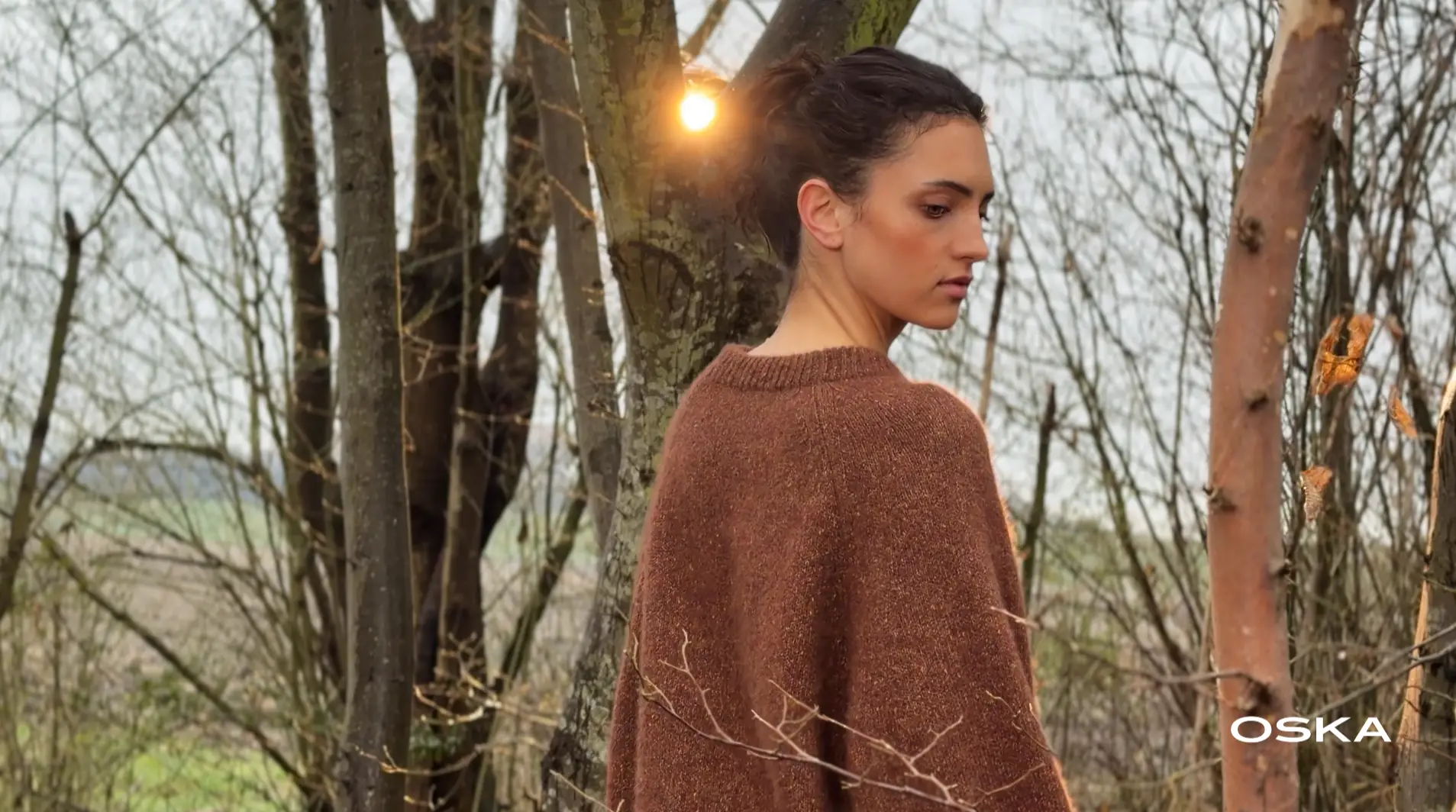 Woman in brown sweater standing in woodland sunlight