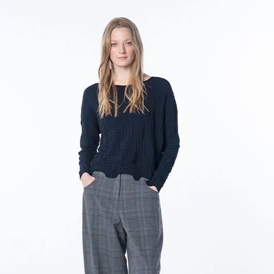 Vrouw in een marineblauwe trui met structuur en een grijze geruite broek