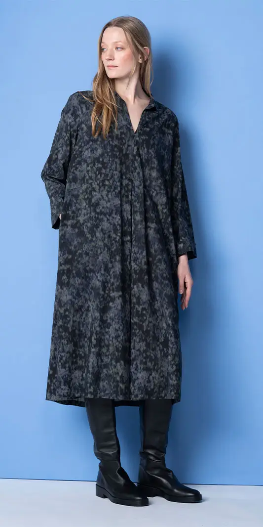 Vrouw in een midi-jurk met print en zwarte kniehoge laarzen.