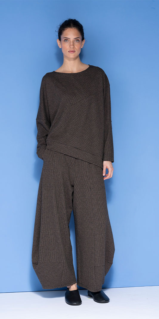 Woman in oversized brown textured tunic and wide-leg trousers.
