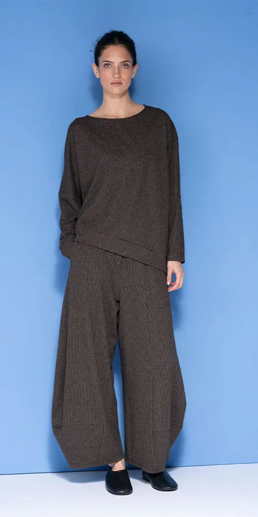 Vrouw in een oversized bruine tuniek met structuur en een wijde broek.