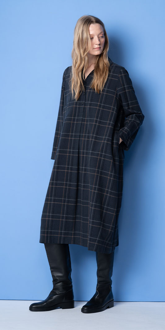 Woman wearing a long plaid shirt dress and black boots.