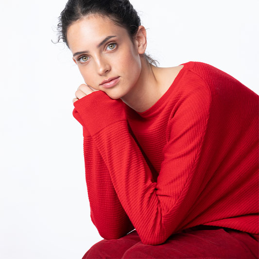 Woman wearing a bright red ribbed sweater against white background