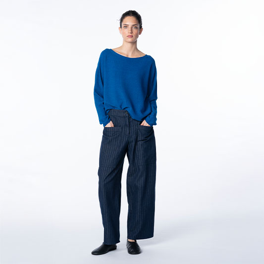Woman wearing a blue sweater and pinstriped wide-leg trousers.