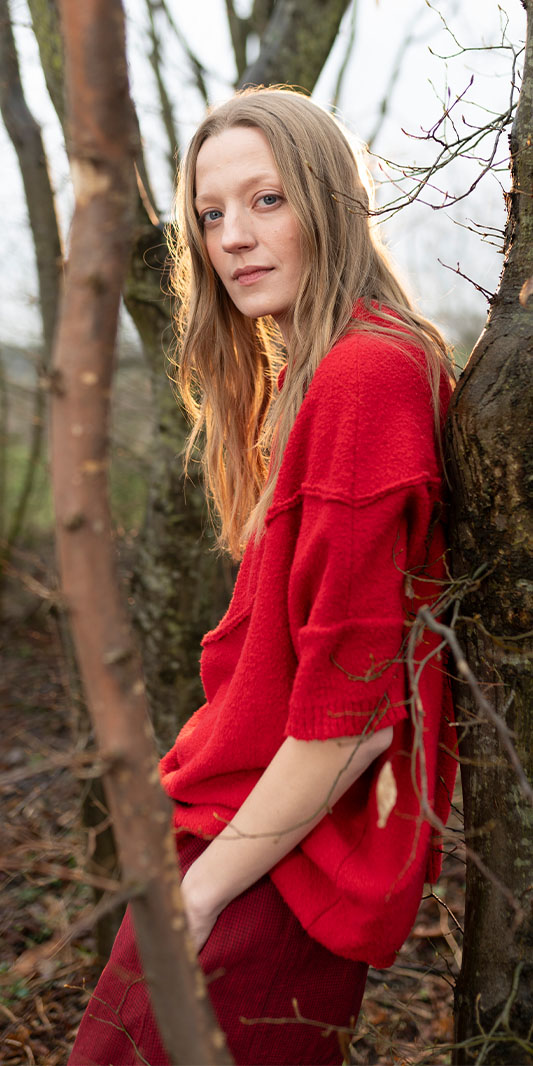 Woman in red sweater leaning against tree in forest.