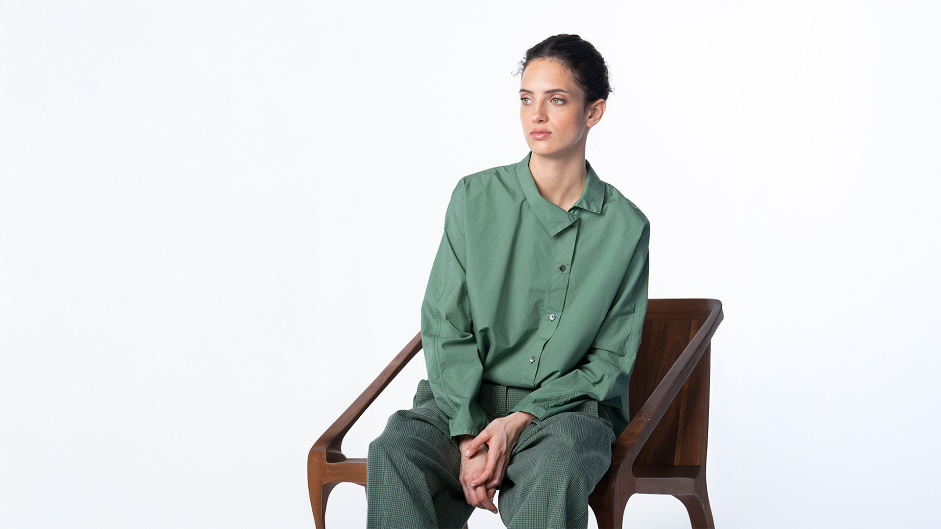 Woman in green shirt and trousers sitting in wooden chair.