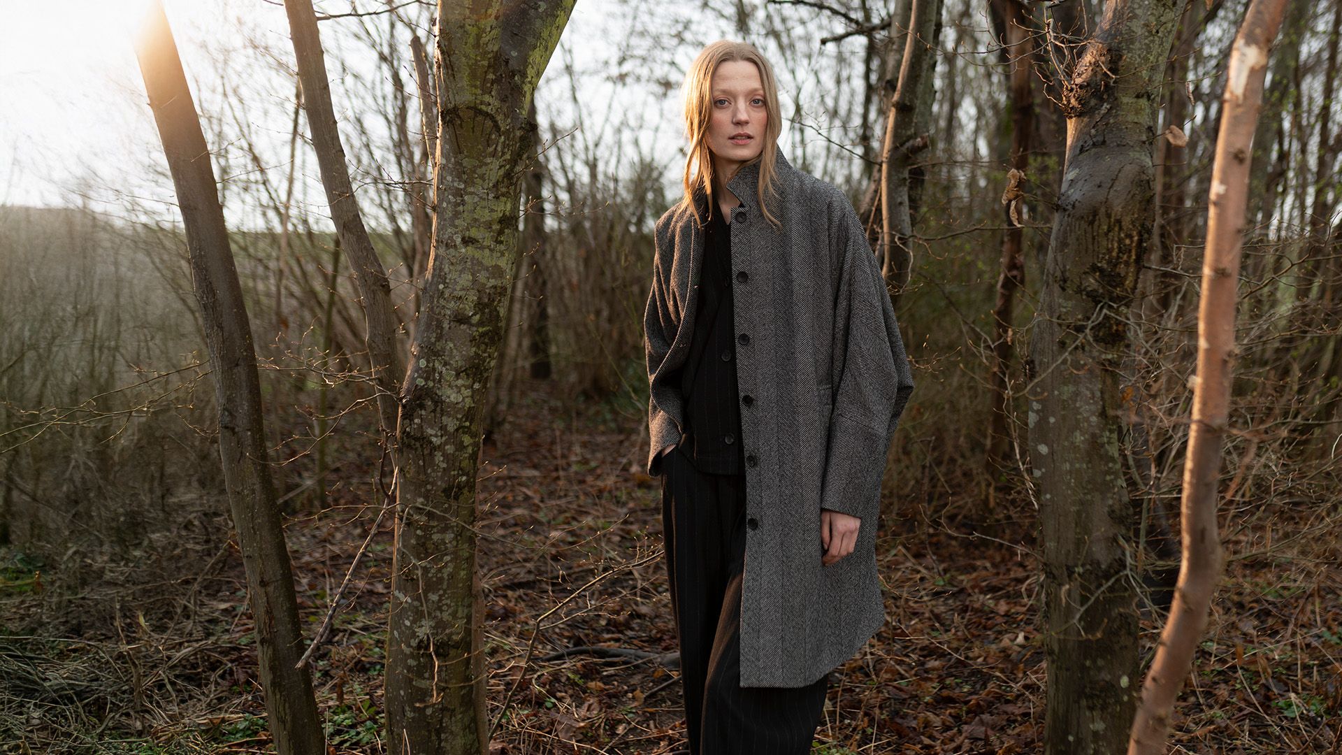Woman in a grey herringbone coat standing in an autumn forest